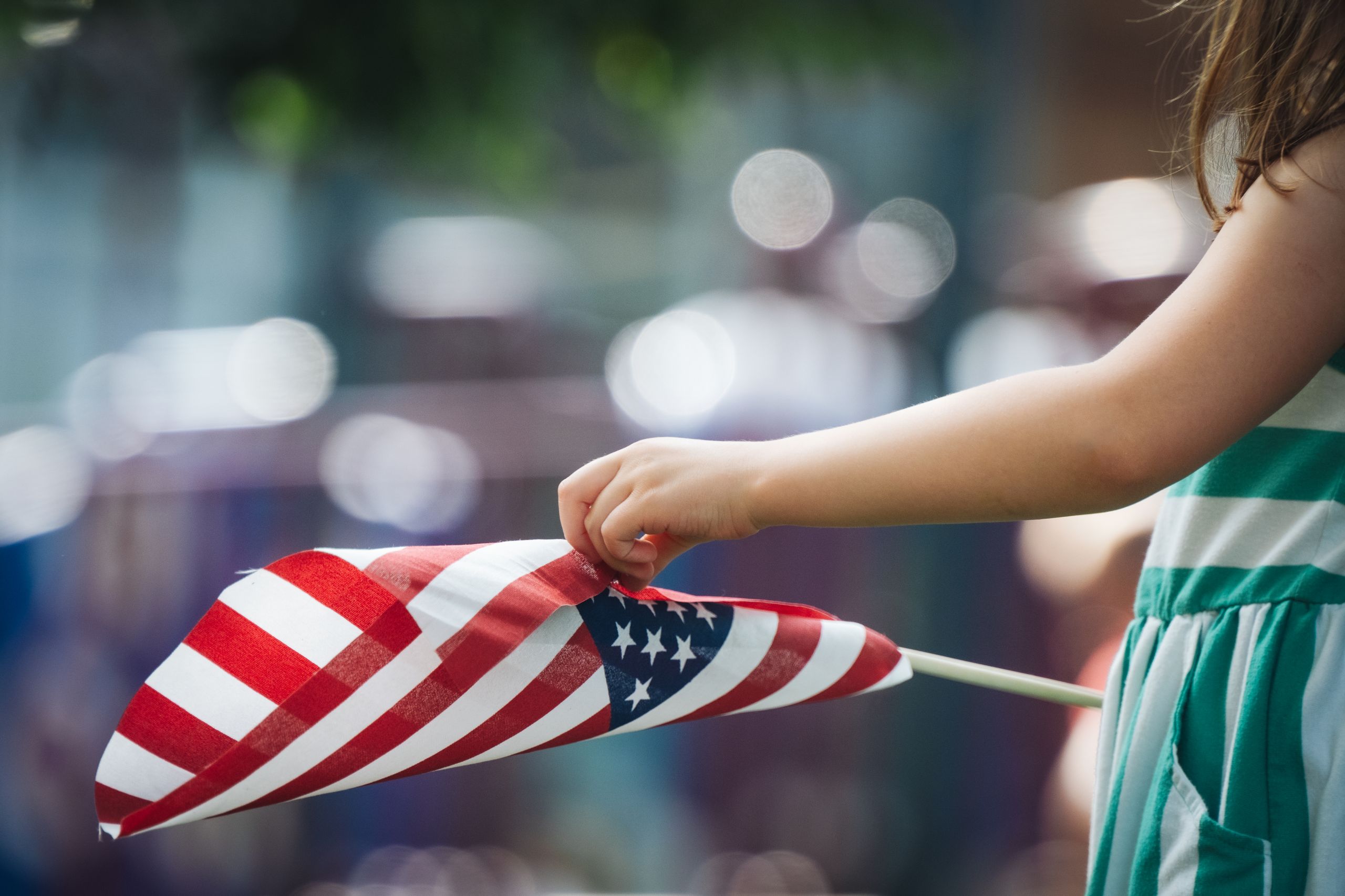 A young girl holding a small American flag outdoors, reflecting patriotism and joy.